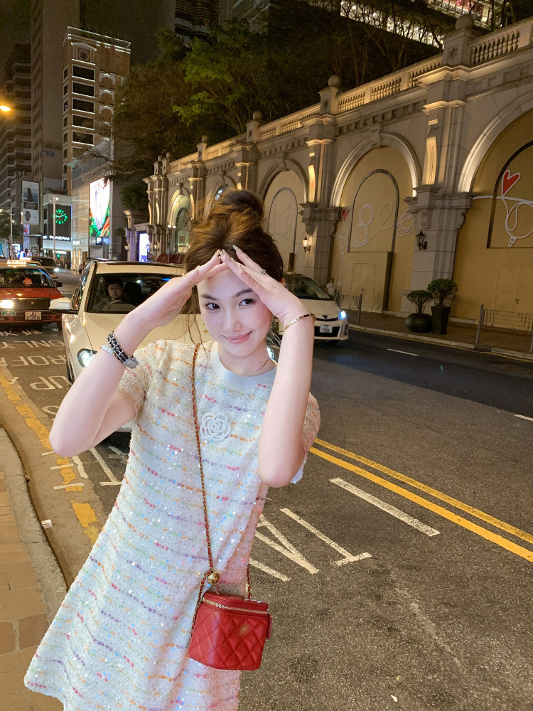 Woman wearing a pastel sequined dress and carrying a red quilted chain bag at night