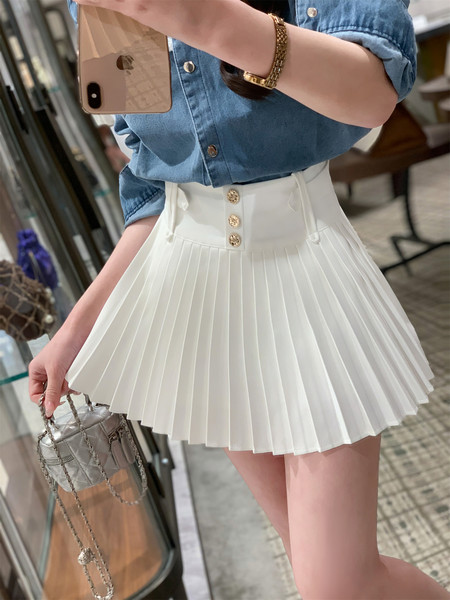 Woman wearing a denim shirt and white pleated mini skirt with a small chain handbag