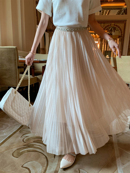 Woman wearing a white pleated dress with a beaded waist and quilted handbag