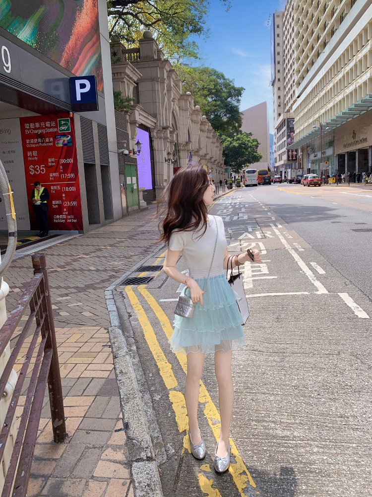 Woman wearing a white top with a light blue layered skirt and silver flats on a city street