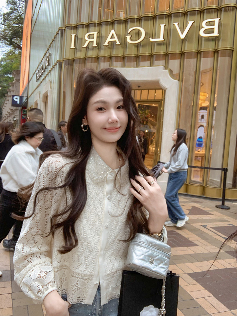 Woman wearing a cream lace blouse with a silver quilted handbag in front of a BVLGARI store