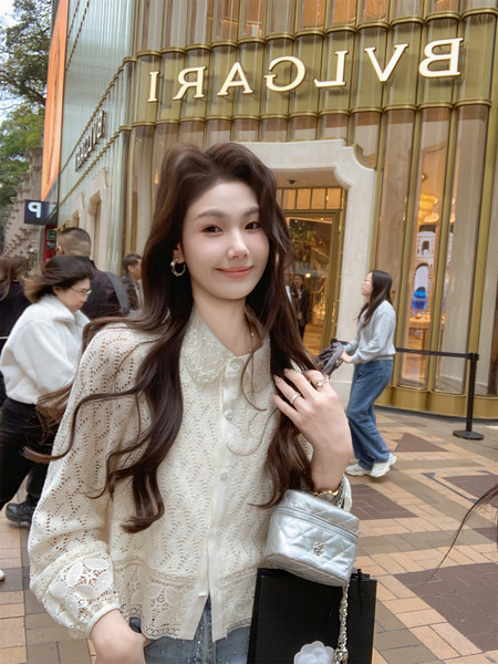Woman wearing a cream lace blouse with a silver quilted handbag in front of a BVLGARI store