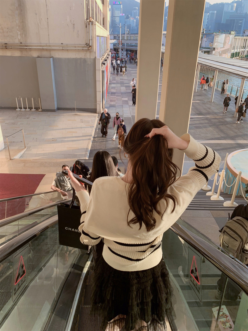 Woman wearing a cream striped sweater and black skirt on an outdoor escalator