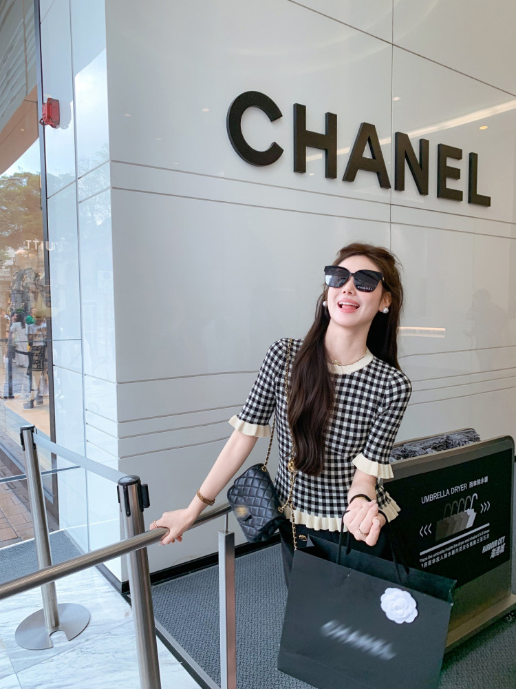 Woman wearing a black-and-white checkered short-sleeve top with ruffle trim and a quilted handbag outside a Chanel store