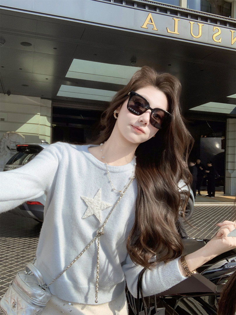 Woman wearing a light blue star-embroidered sweater and black sunglasses outdoors