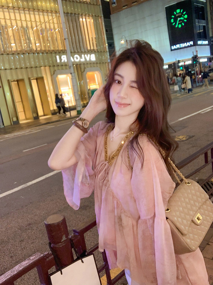 Woman wearing a pink sheer outfit with a beige quilted handbag at night