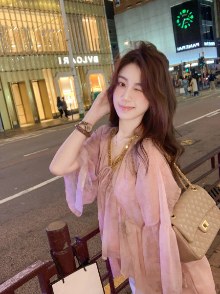 Woman wearing a pink sheer outfit with a beige quilted handbag at night