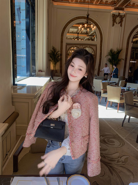 Woman wearing a pink tweed jacket with a black handbag in an elegant restaurant setting