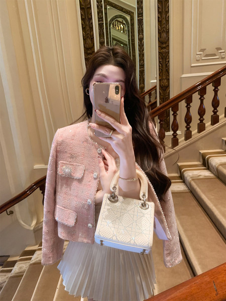 Woman wearing a pink tweed jacket and holding a cream handbag