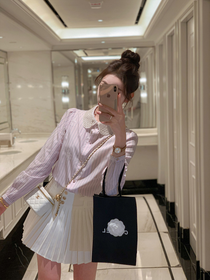 Woman wearing a pastel striped blouse with a pleated skirt in a mirror selfie