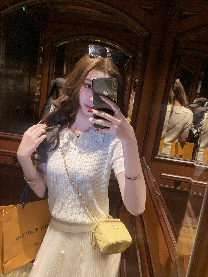 Woman wearing a white lace knit top with a pleated skirt and a small yellow crossbody bag in a mirror selfie