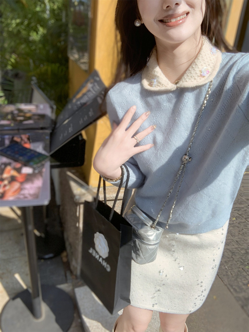 Woman wearing a light blue knit top with a pearl-accent skirt and chain bag