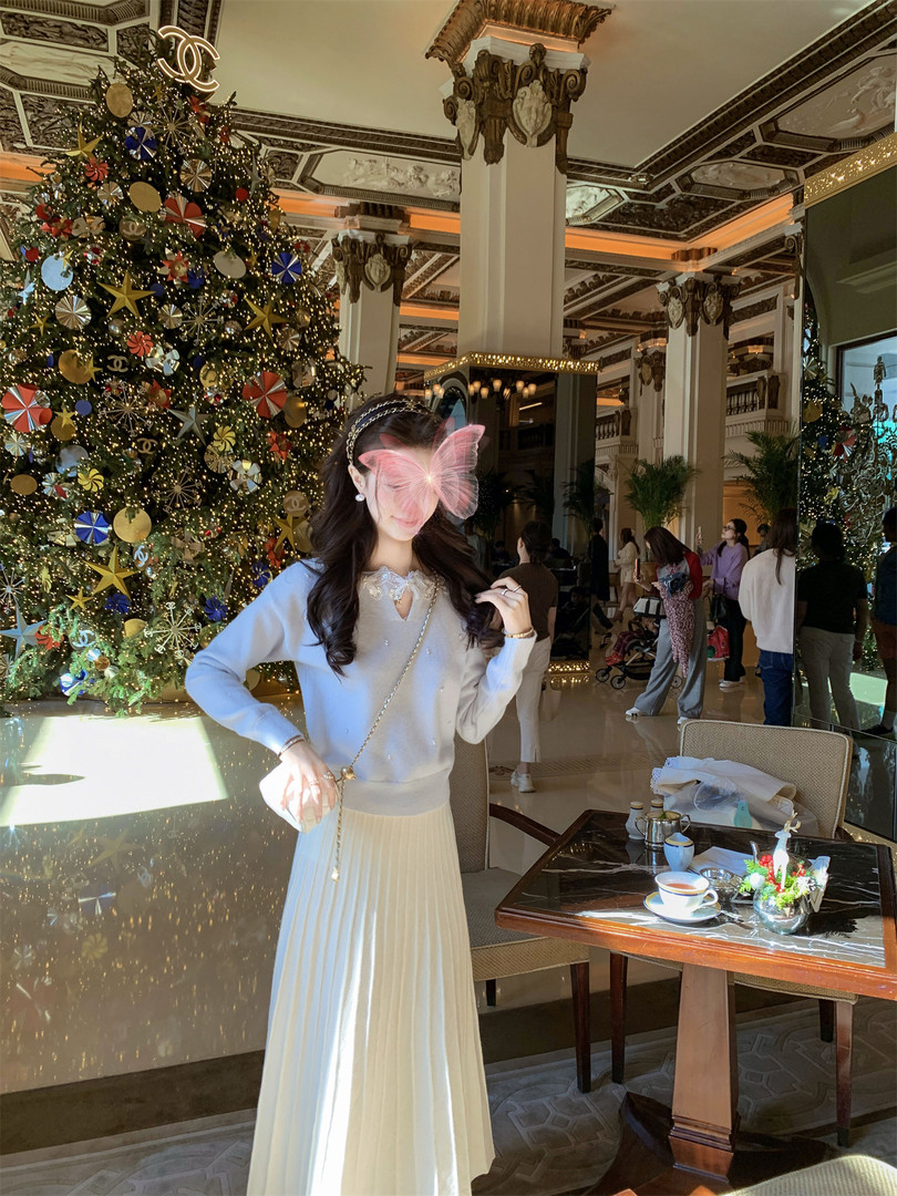 Woman wearing a light blue sweater and cream pleated skirt in a festive holiday setting
