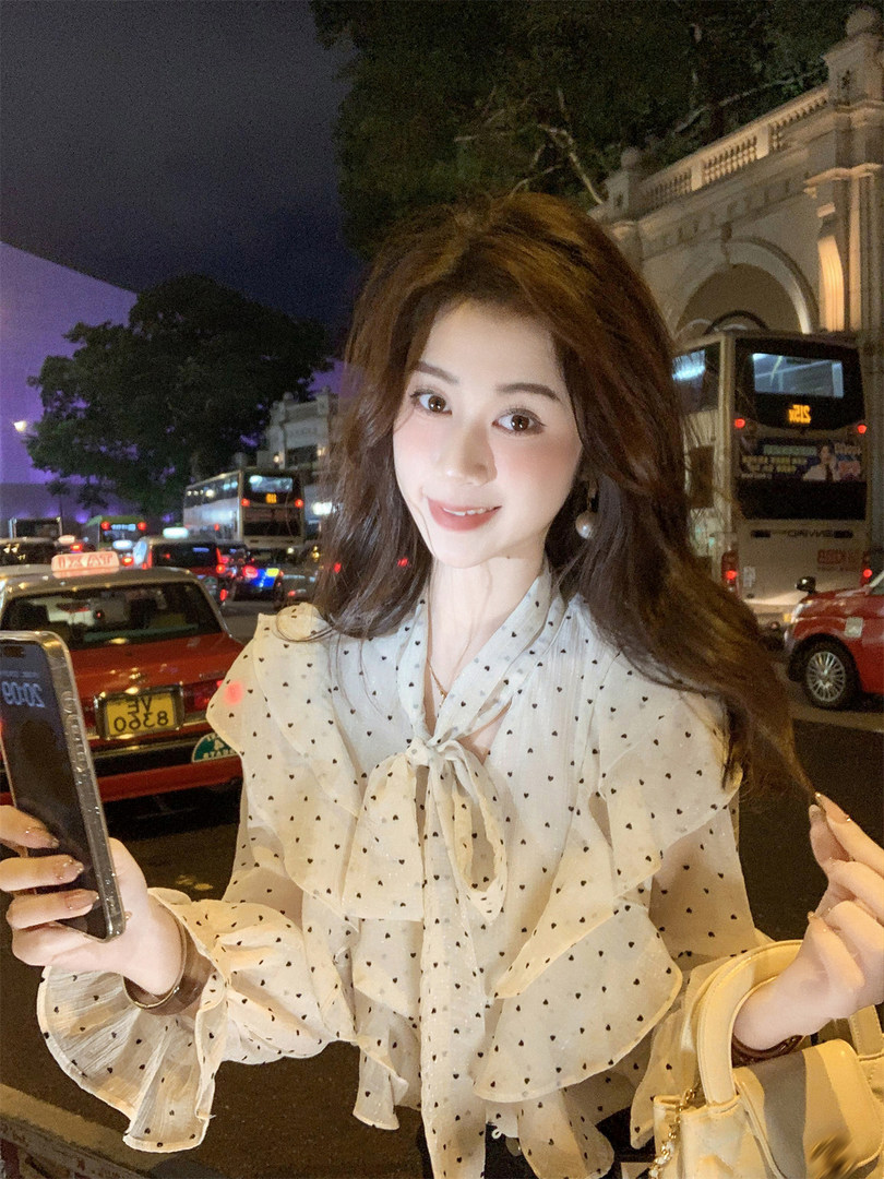 Woman wearing a sheer polka dot bow blouse at night on a city street
