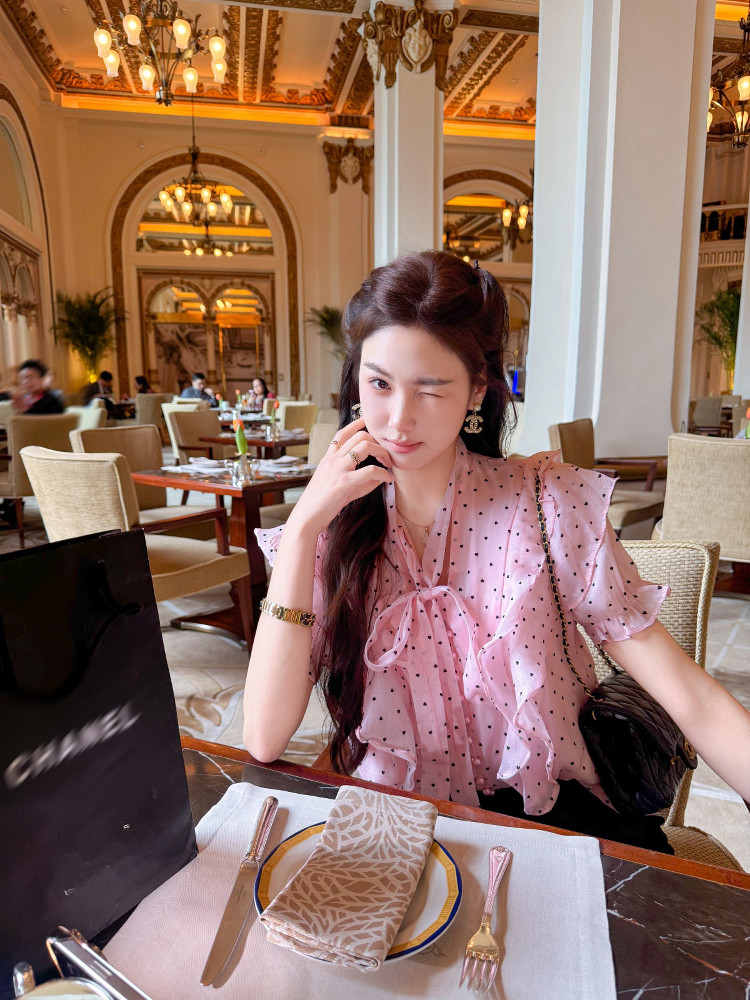 Woman wearing a pink sheer polka dot ruffled blouse at a restaurant