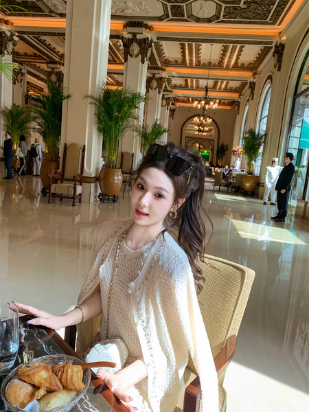 Woman wearing a light cream lace knit outfit with a sheer cape cardigan in an elegant restaurant setting