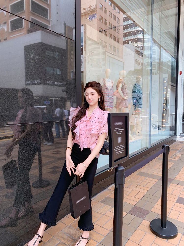 Woman wearing a pink ruffled polka dot blouse with black flared pants outdoors