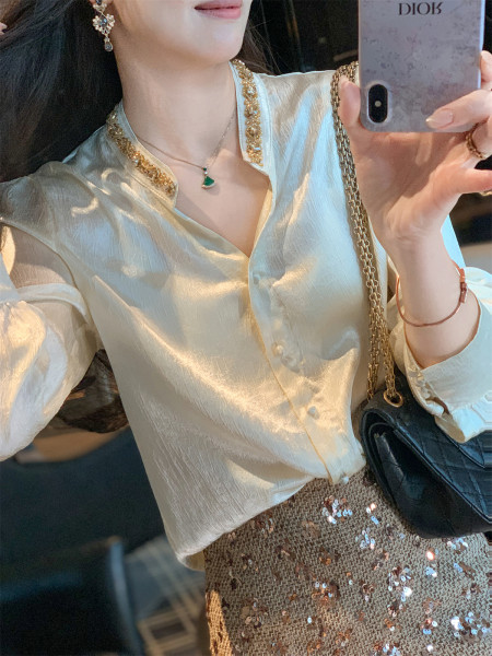 Woman wearing a cream satin blouse with gold trim and a sequined skirt, holding a black chain bag