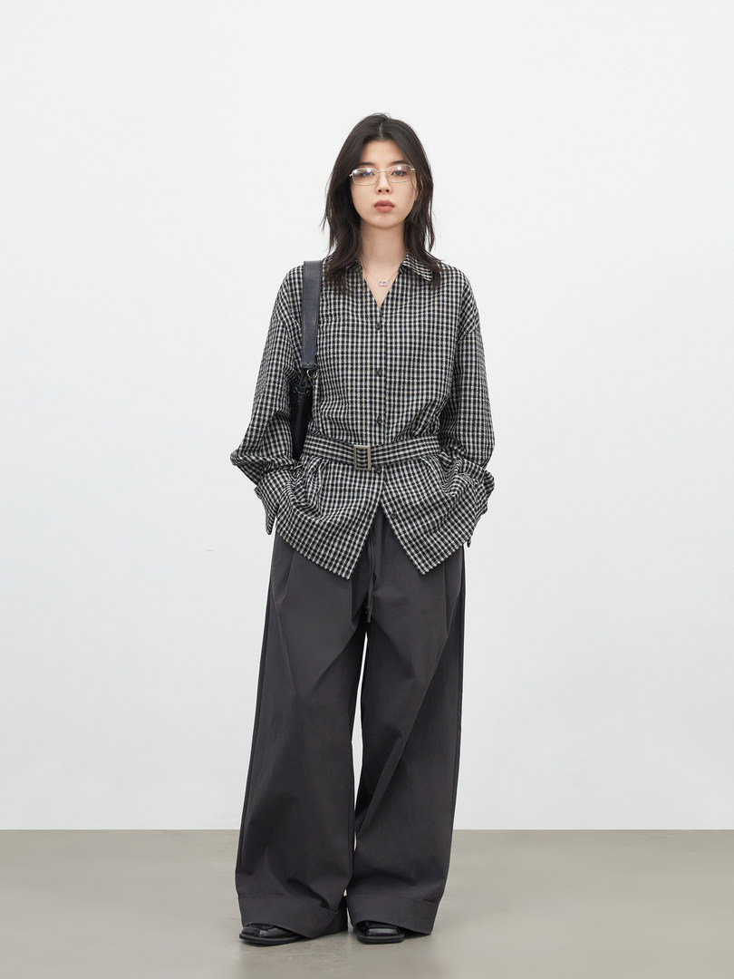 Model wearing a black-and-white checkered shirt with wide-leg dark pants and a belt