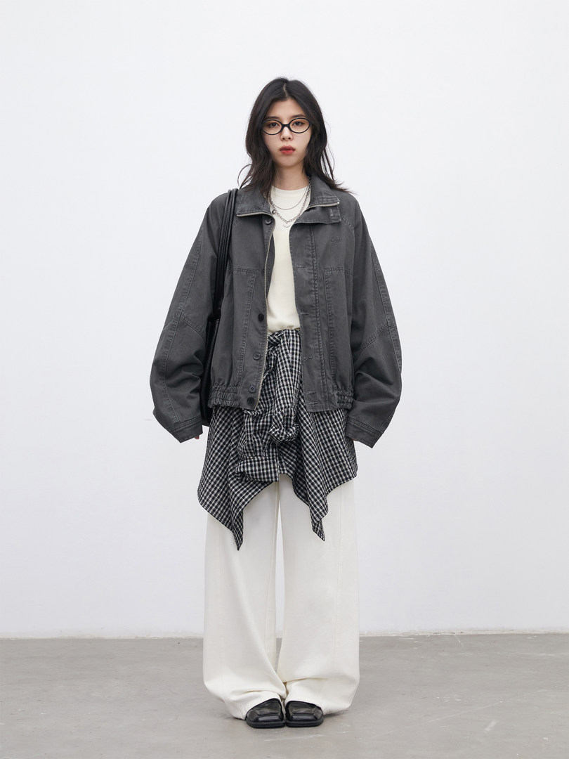 Model wearing a dark gray jacket layered over a checkered top with white wide-leg pants