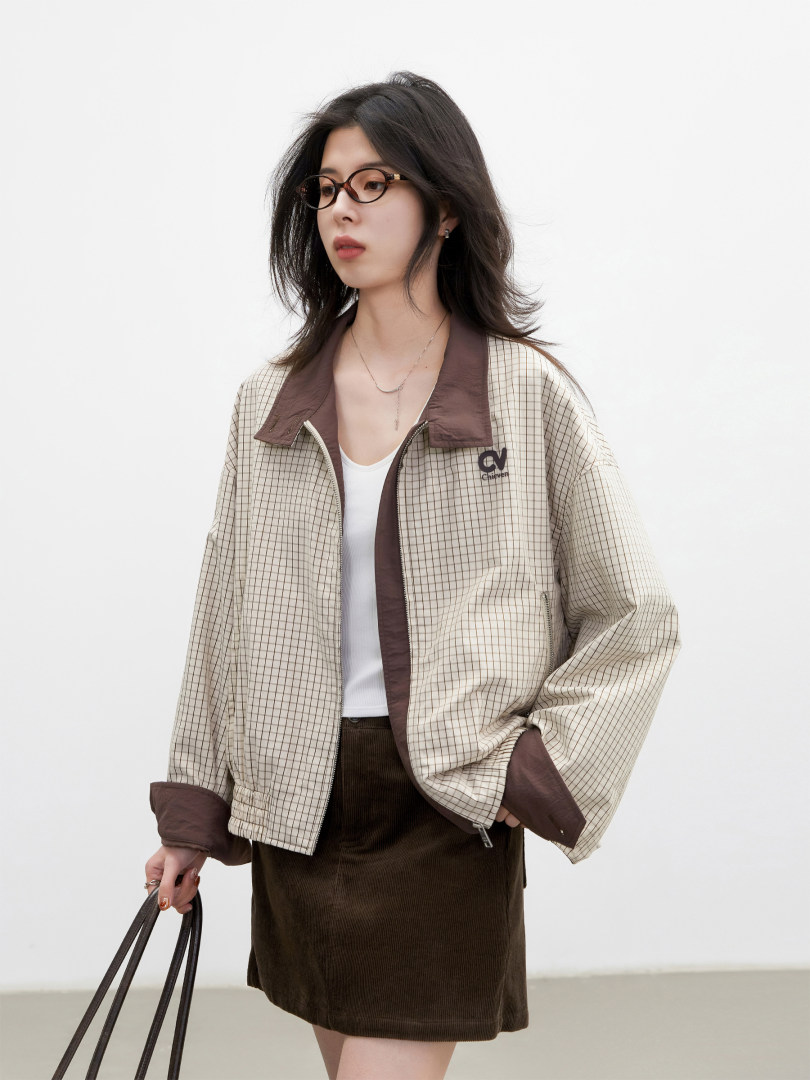 Model wearing a checkered zip-up jacket with brown trim and a dark skirt