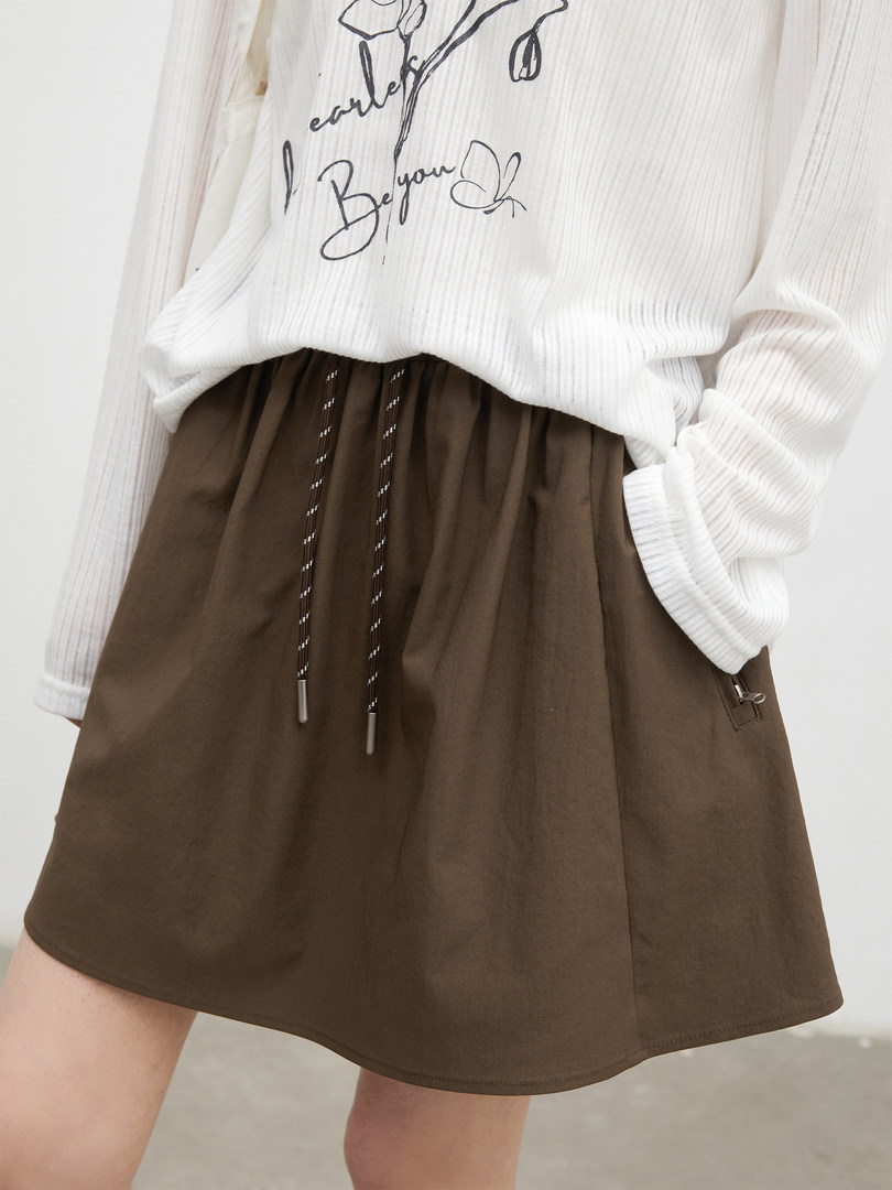 Brown mini skirt worn with a white long-sleeve graphic top on a model