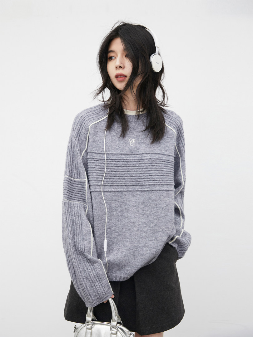 Model wearing a gray knit sweater with white piping and headphones