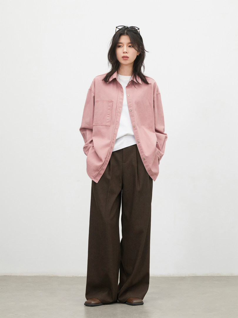 Model wearing a pink button-up shirt with wide brown pants on a plain white background