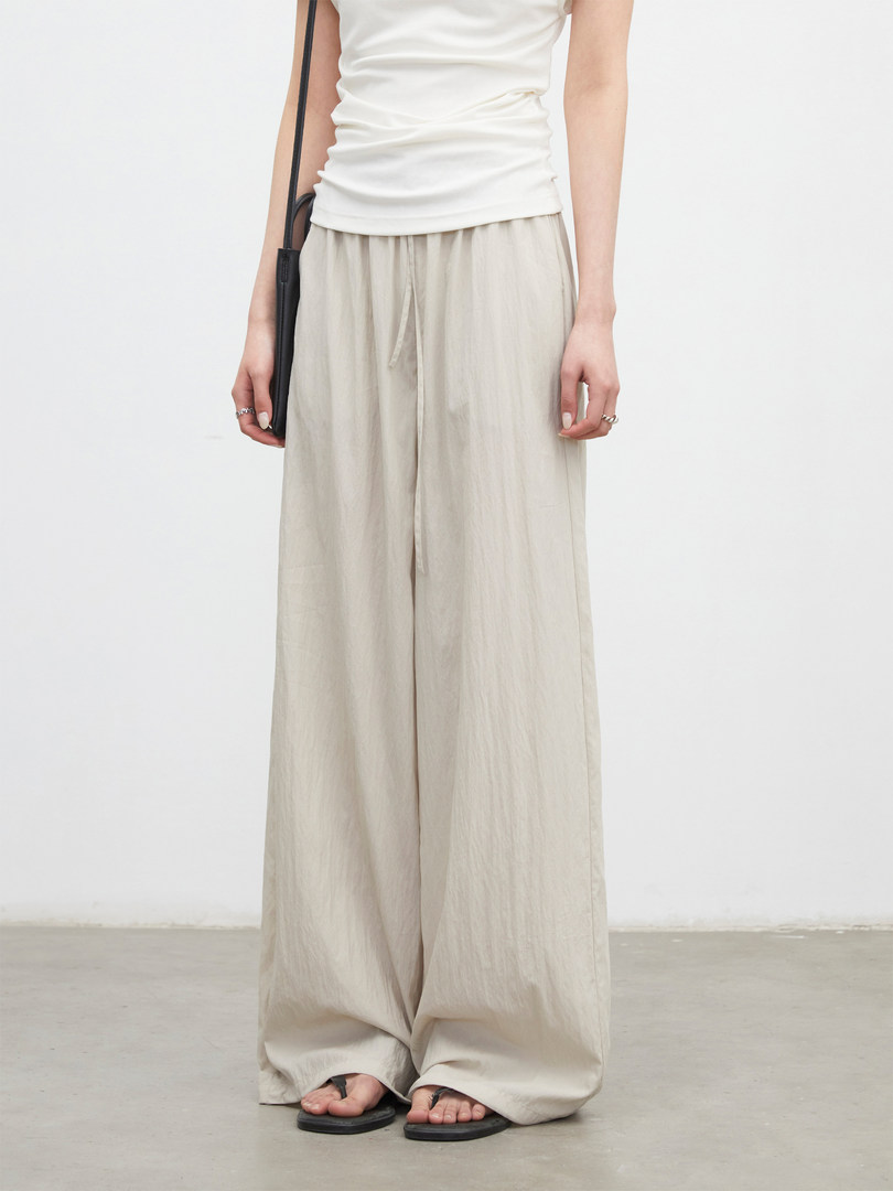 Model wearing cream wide-leg pants with a white top and black sandals