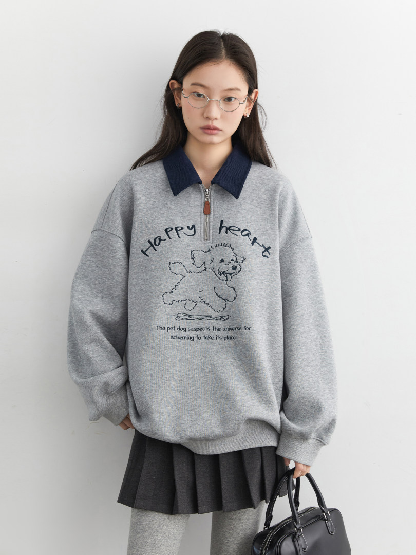 Model wearing a gray graphic half-zip sweatshirt with a pleated skirt and black handbag