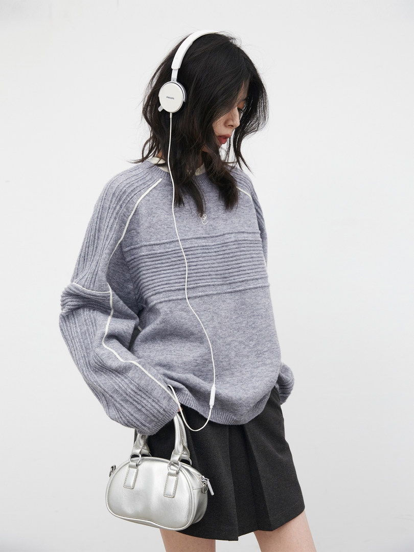 Model wearing a gray knit sweater with white headphones and a silver handbag