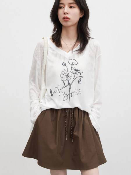 Model wearing a white graphic long-sleeve top with a brown skirt