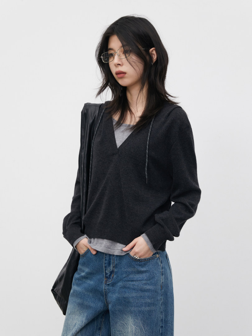 Model wearing a black knit sweater layered over a gray tee with blue jeans