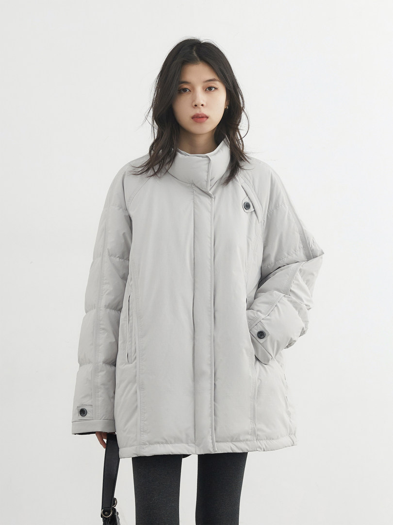 Woman wearing a light gray puffer coat on a plain background