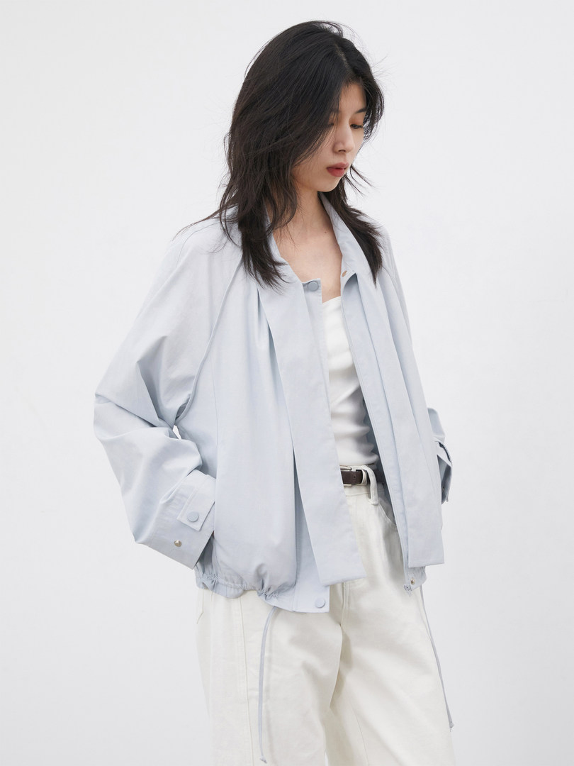 Model wearing a light gray oversized jacket with white pants on a plain background