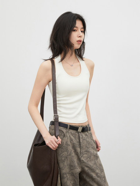 Model wearing a white tank top with patterned pants and a brown shoulder bag
