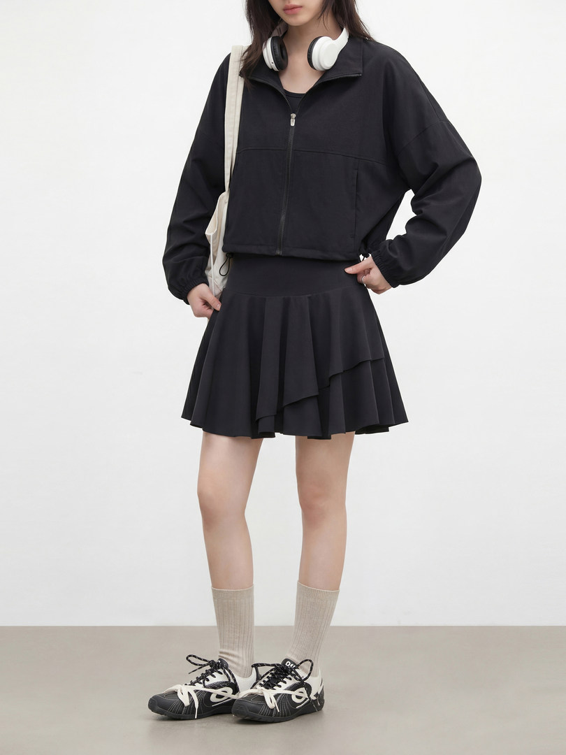 Model wearing a black zip-up jacket with a pleated skirt and sneakers