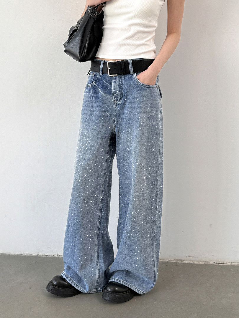 Model wearing wide-leg glittery blue jeans with a black belt and white tank top