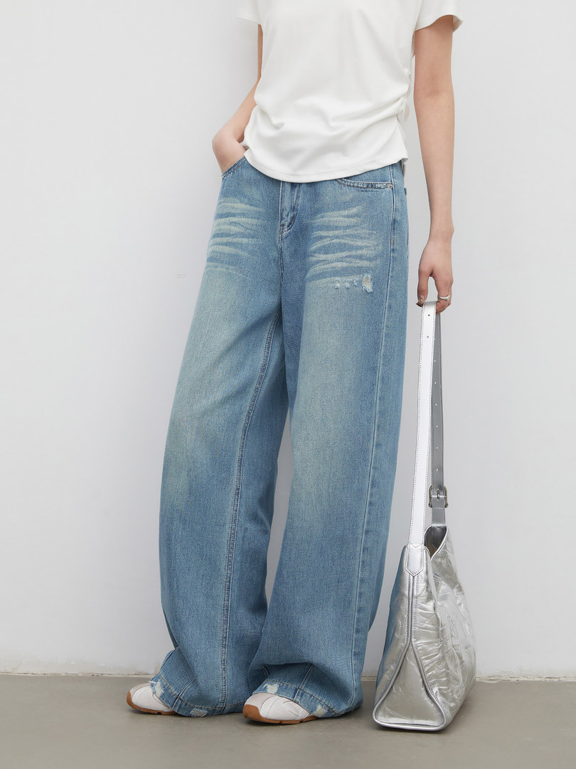 Model wearing wide-leg distressed blue jeans with a white top and silver shoulder bag