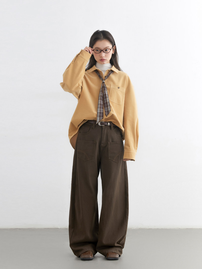 Model wearing a tan long-sleeve shirt with plaid tie and brown wide-leg pants