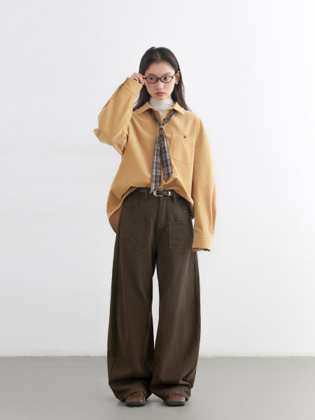 Model wearing a tan long-sleeve shirt with plaid tie and brown wide-leg pants