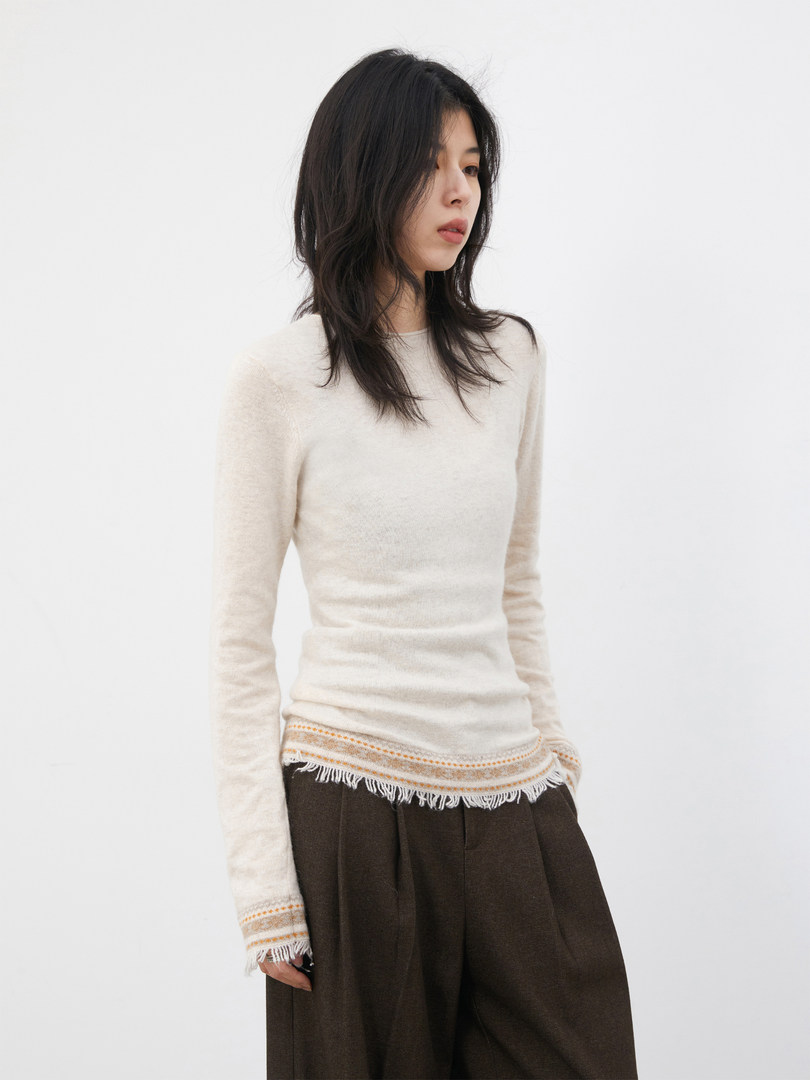 Model wearing a cream long-sleeve knit top with fringe hem and dark wide-leg pants
