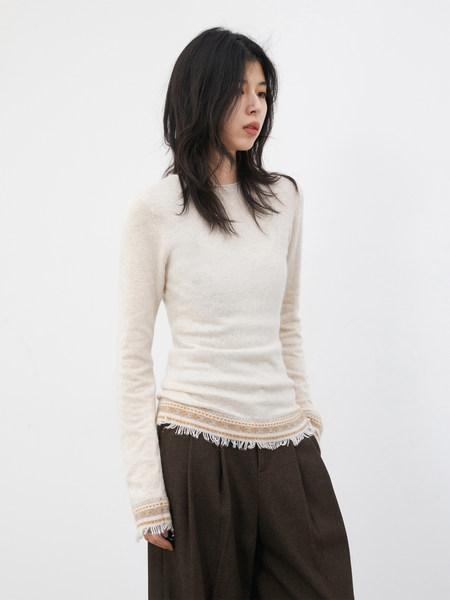 Model wearing a cream long-sleeve knit top with fringe hem and dark wide-leg pants
