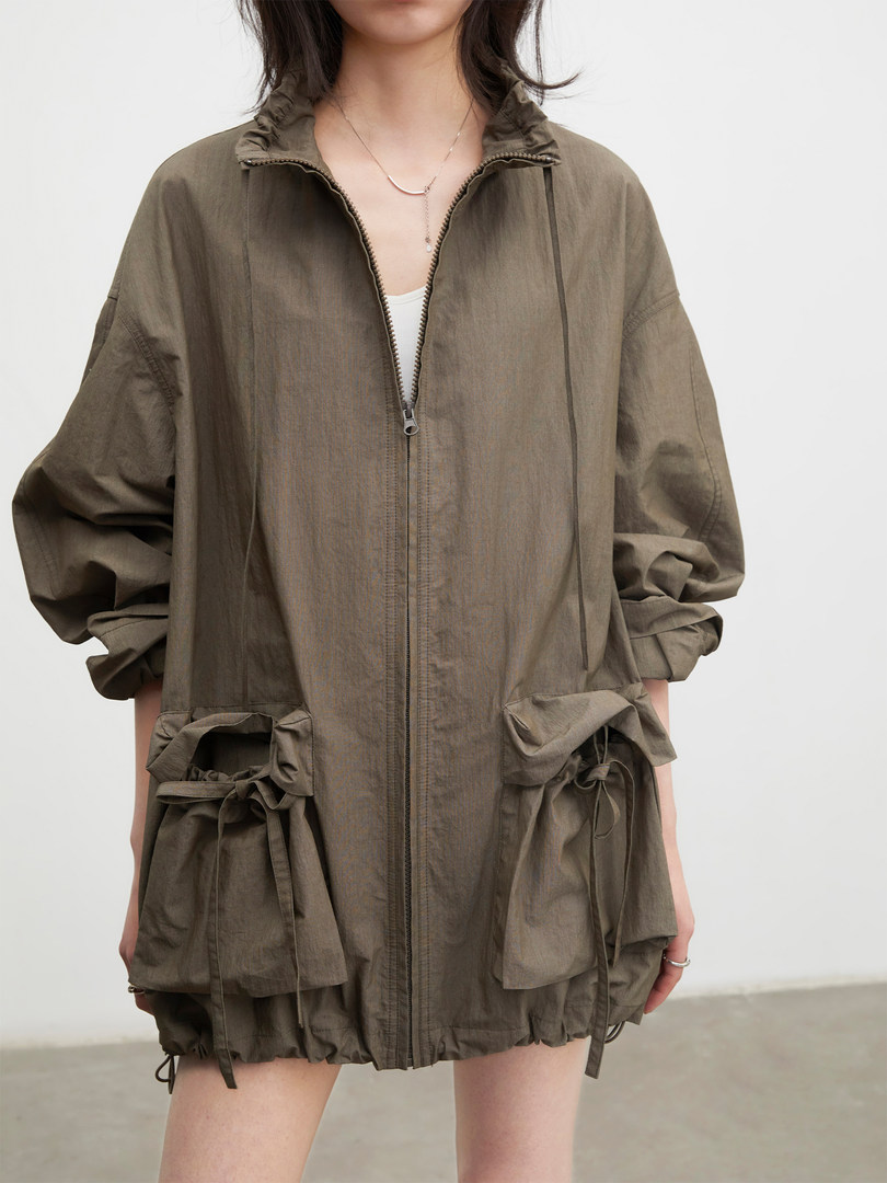 Model wearing an oversized olive zip-up lightweight jacket with drawstring pockets