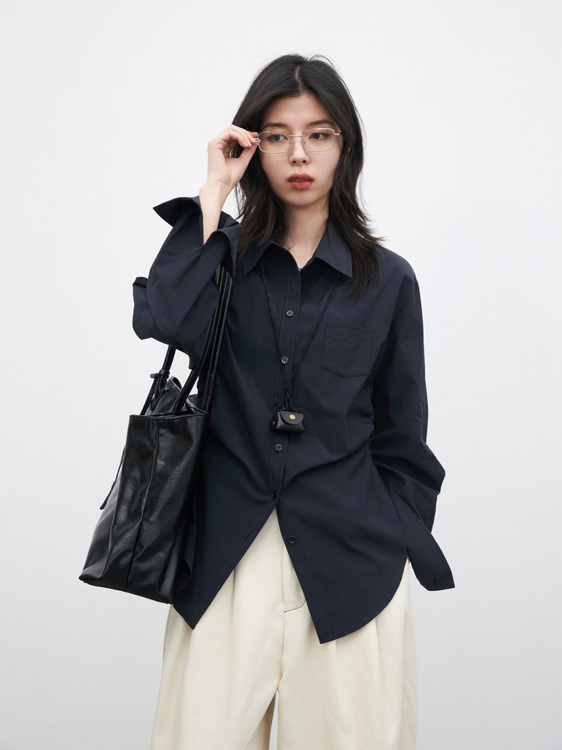 Model wearing a navy button-up shirt with cream pants and a black tote bag