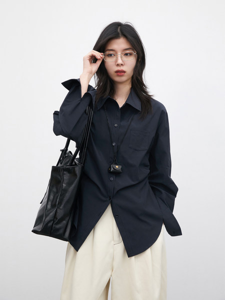 Model wearing a navy button-up shirt with cream pants and a black tote bag