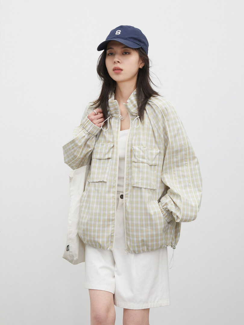 Model wearing a light plaid zip-up jacket with white shorts and a navy cap
