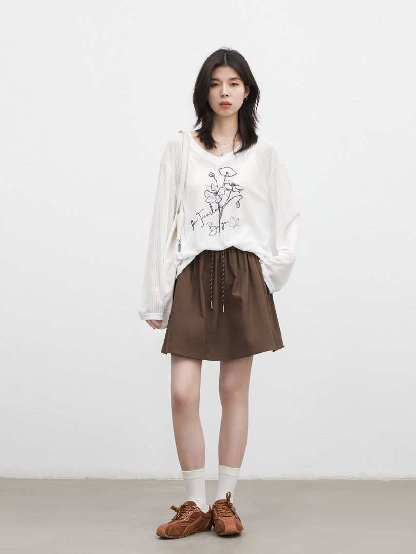 Model wearing a white printed long-sleeve top with a brown mini skirt and brown sneakers