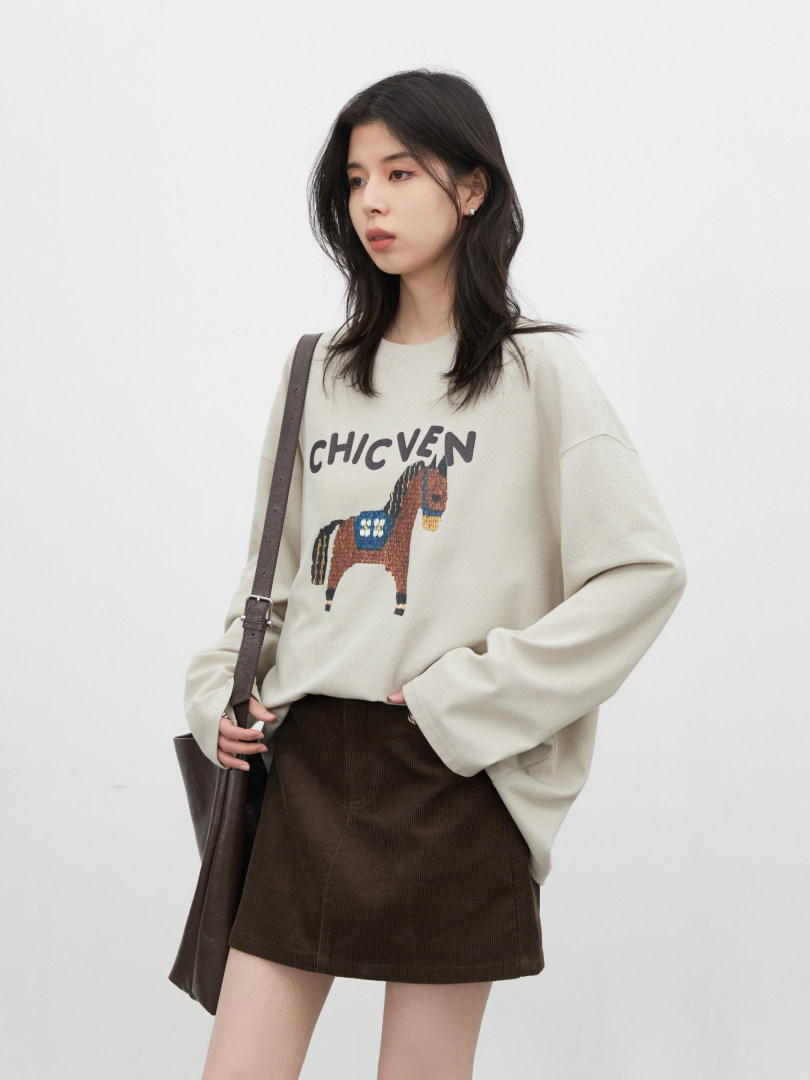 Model wearing an oversized cream sweatshirt with a horse graphic and brown mini skirt