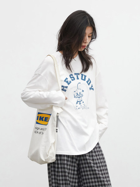 Model wearing a white graphic sweatshirt with a tote bag and plaid pants